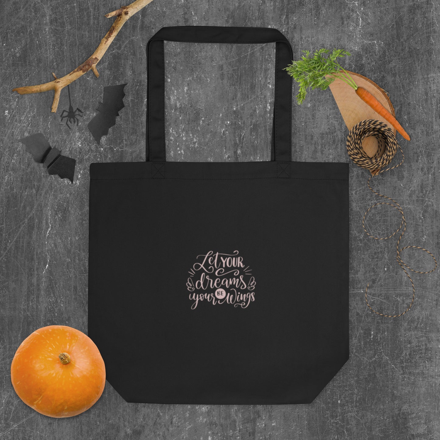Black tote bag with 'Let your dreams be your wings' text on a gray surface with vegetables.